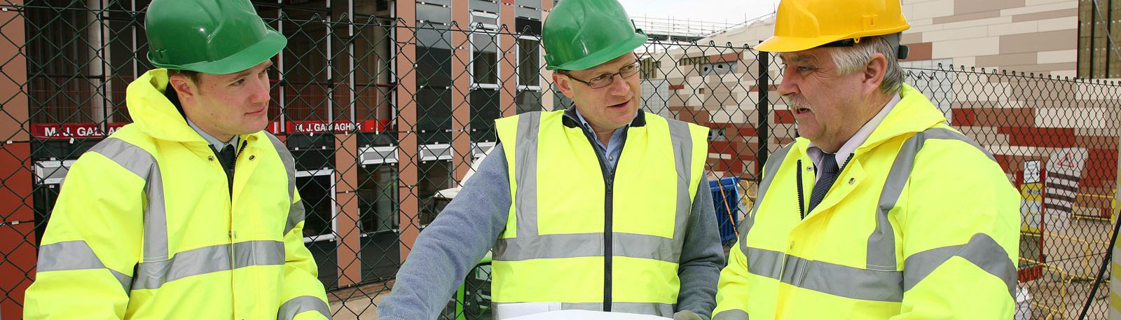 Three men studying construction plans wearing high-vis jackets and hard hats