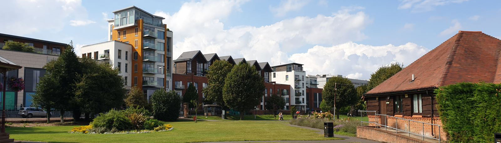 Open greenspace with a small building to the side and modern apartment block in the background